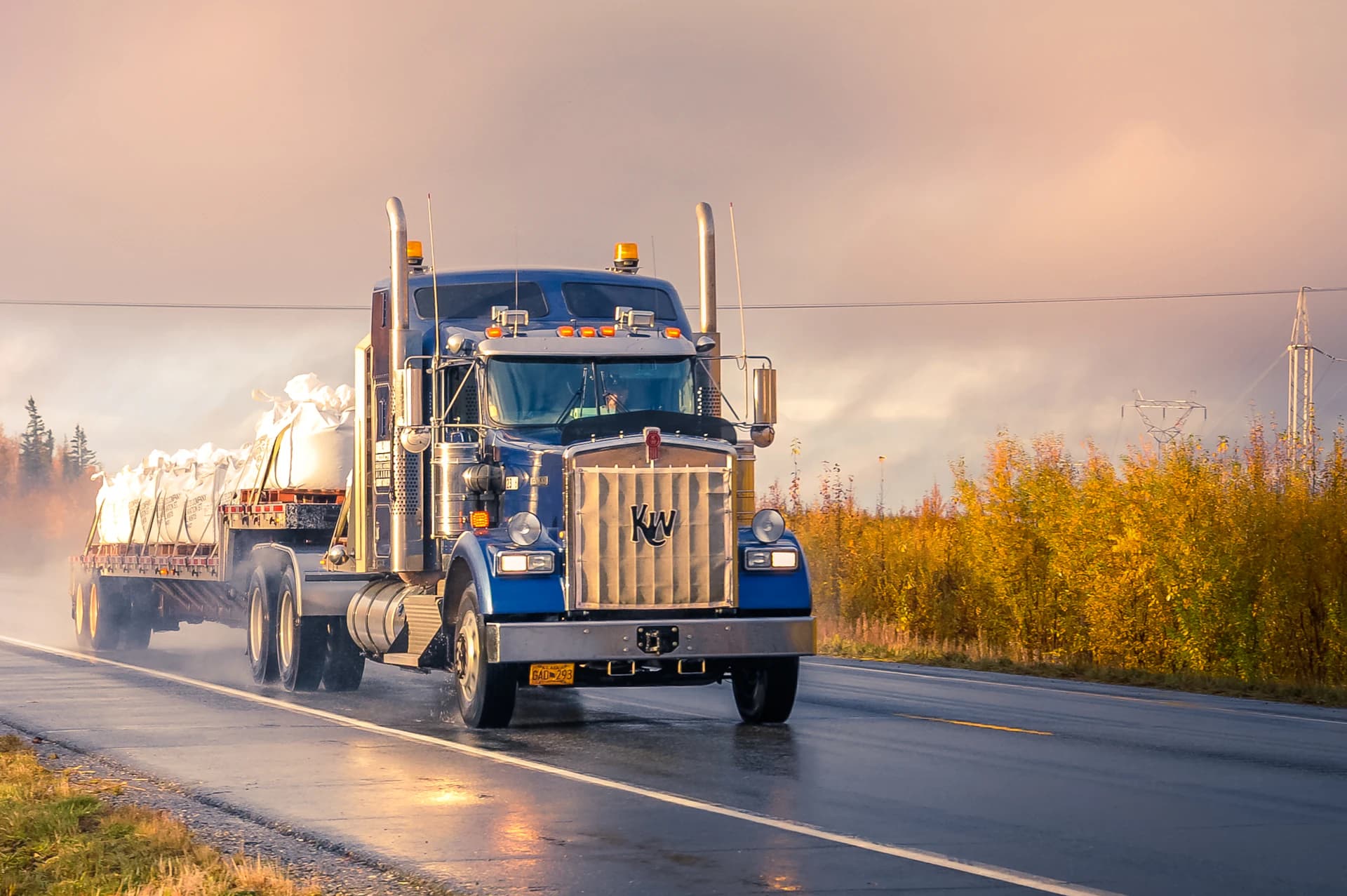 Semi truck hauling freight on a wet highway at sunrise